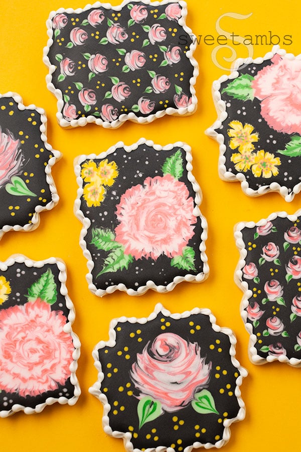 a set of plaque cookies decorated with pink and yellow flowers on black royal icing. The cookies are on a golden yellow background.