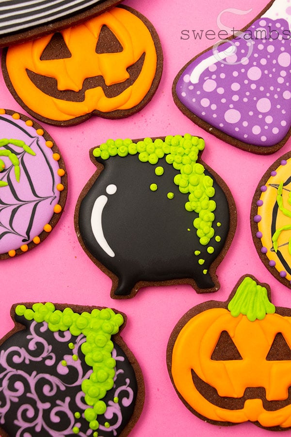 Brightly colored Halloween cookies decorated to look like a jack-o'lantern, spider webs with neon green spiders, a bubbling cauldron, and a science beaker