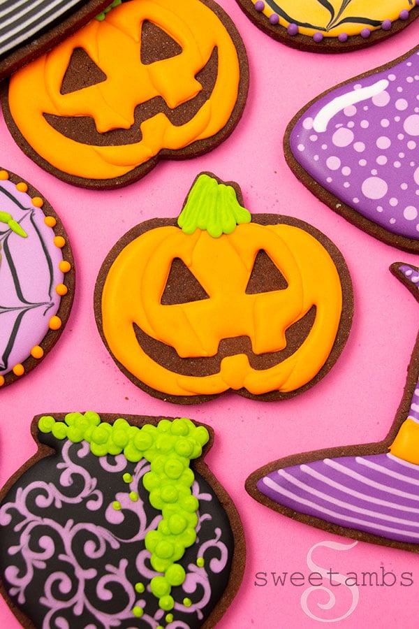 A cookie decorated to look like a jack-o'lantern. The cookie is surrounded by brightly colored Halloween cookies.