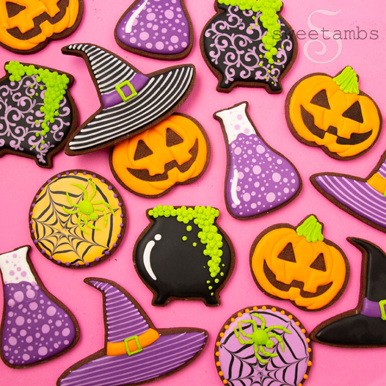 Brightly colored Halloween cookies decorated to look like a jack-o'lantern wearing a striped witch hat, spider webs with neon green spiders, a bubbling cauldron, and a science beaker