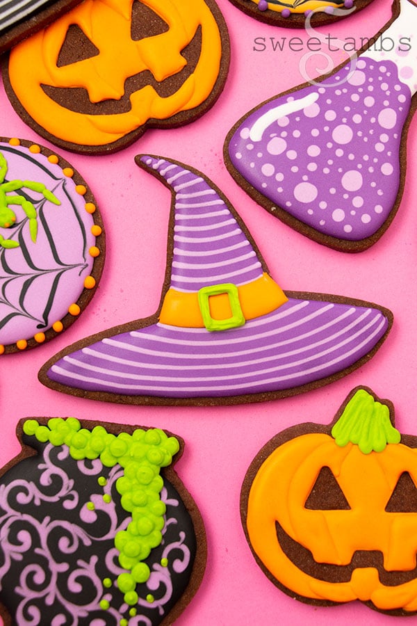 Brightly colored Halloween cookies decorated to look like a striped witch hat, a jack-o'lantern, spider webs with neon green spiders, a bubbling cauldron, and a science beaker
