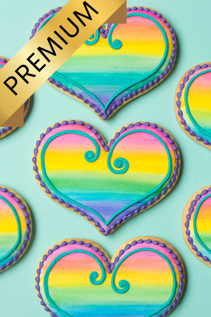 3 heart cookies decorated with a rainbow watercolor design. The work Premium is in a gold banner across the top left corner of the image.