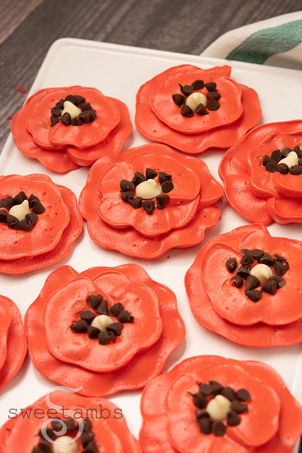 Meringue poppies on a plate over a wooden backdrop with a green and white striped dish towel on the left side of the plate