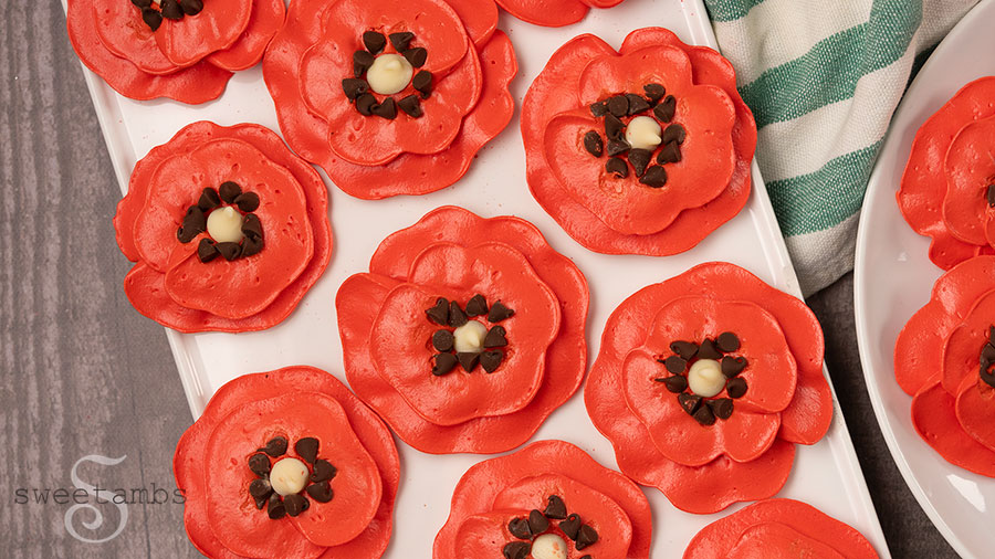Meringue poppies on a plate over a wooden backdrop with a green and white striped dish towel on the left side of the plate