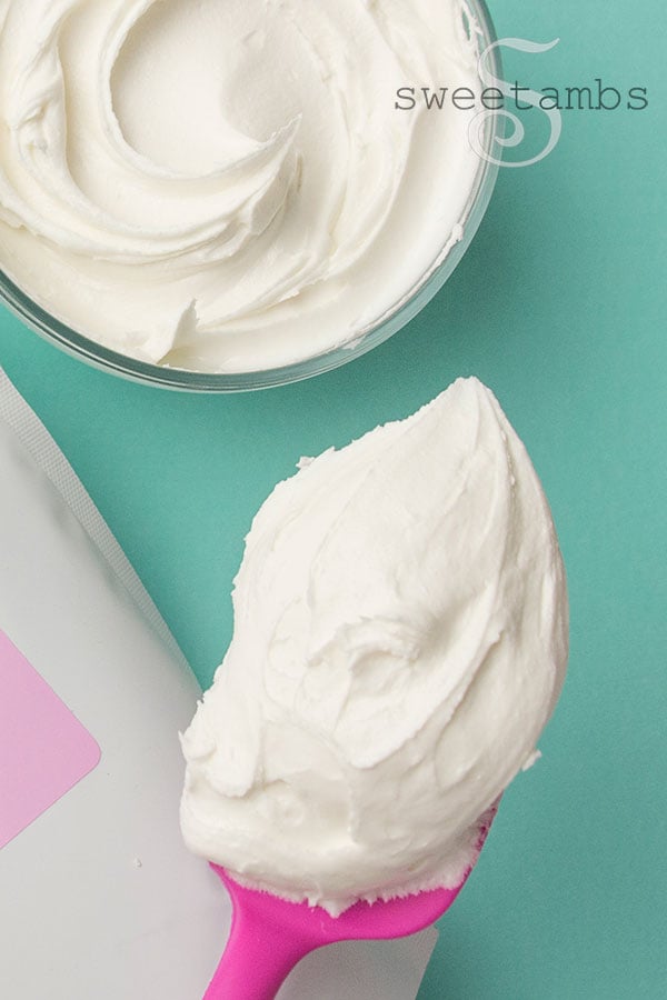 A spatula with a dollop of icing. There is a bowl of icing in the background