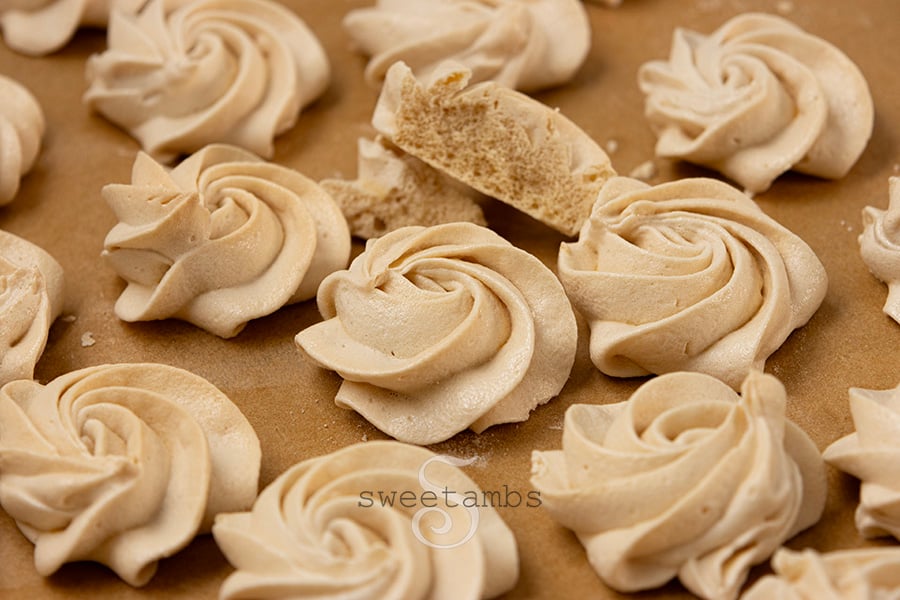 Swirled brown sugar meringue cookies on unbleached parchment paper. One of the meringue cookies is broken in half, showing the texture inside.