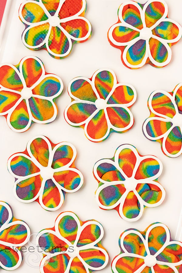flower shaped cookies made from swirled rainbow cookie dough with white icing outlines.