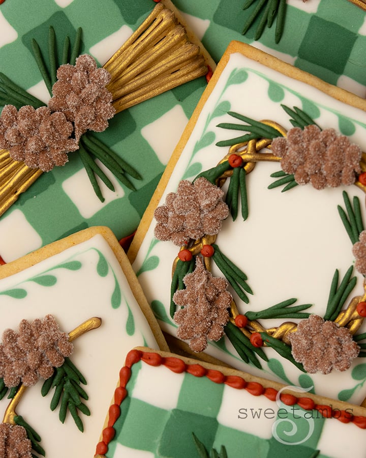 A close up of a set of square decorated cookies decorated with royal icing in green and white plaid, pine cones, wreaths, and boughs.