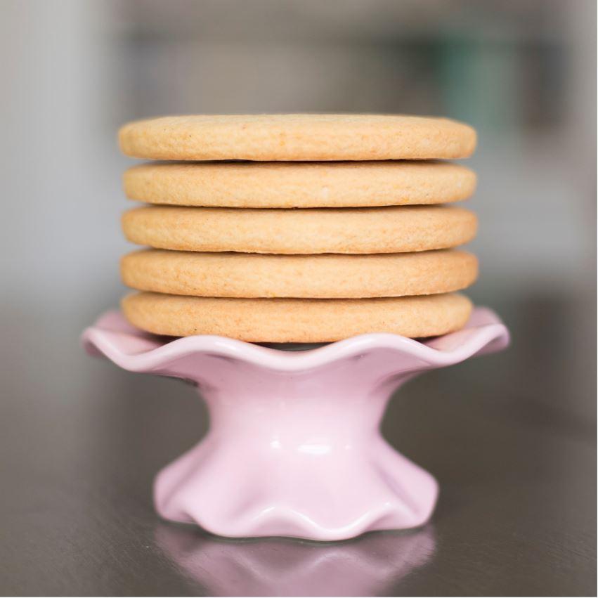 A stack of plain cookies sits on a pink ruffled cake plate