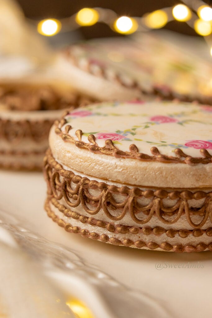 A side view of the cookies decorated to resemble vintage floral enameled makeup compacts, showing the piped lace detail. There are bokeh fairy lights in the background.