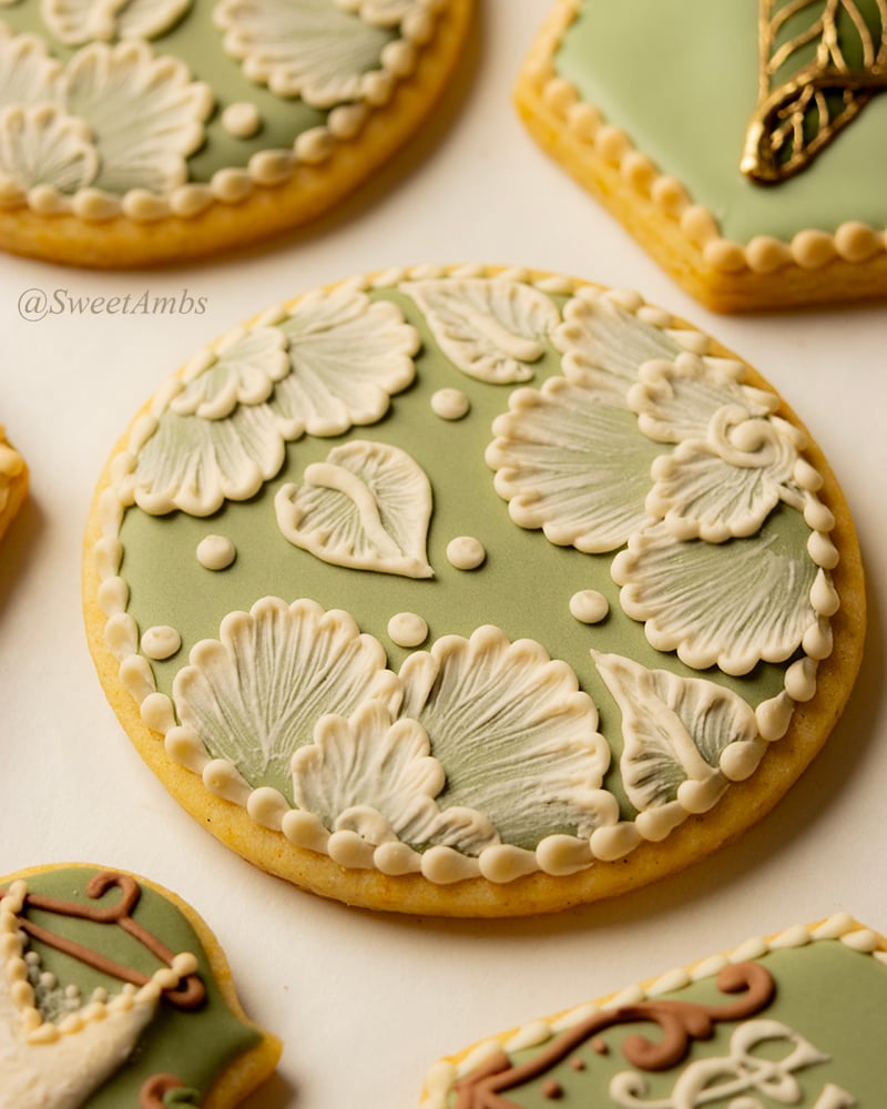 A round cookie decorated with a layer of light green icing and ivory brush embroidered flowers.