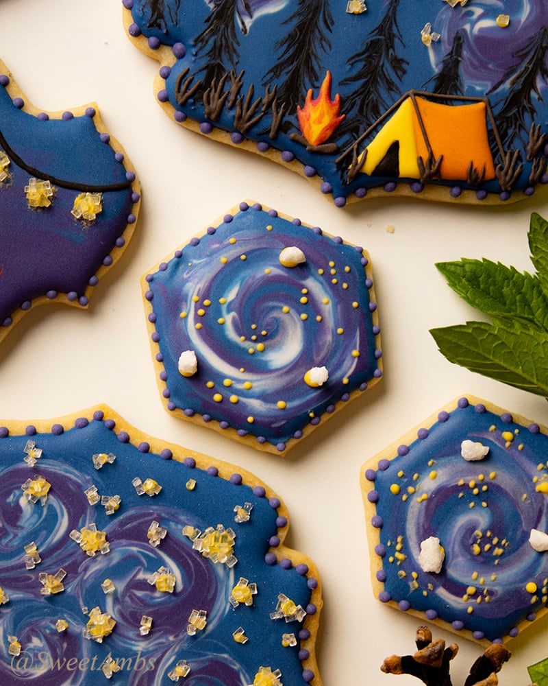 A hexagon shaped cookie decorated with a galaxy design. The cookie is inspired by camping design cookies.