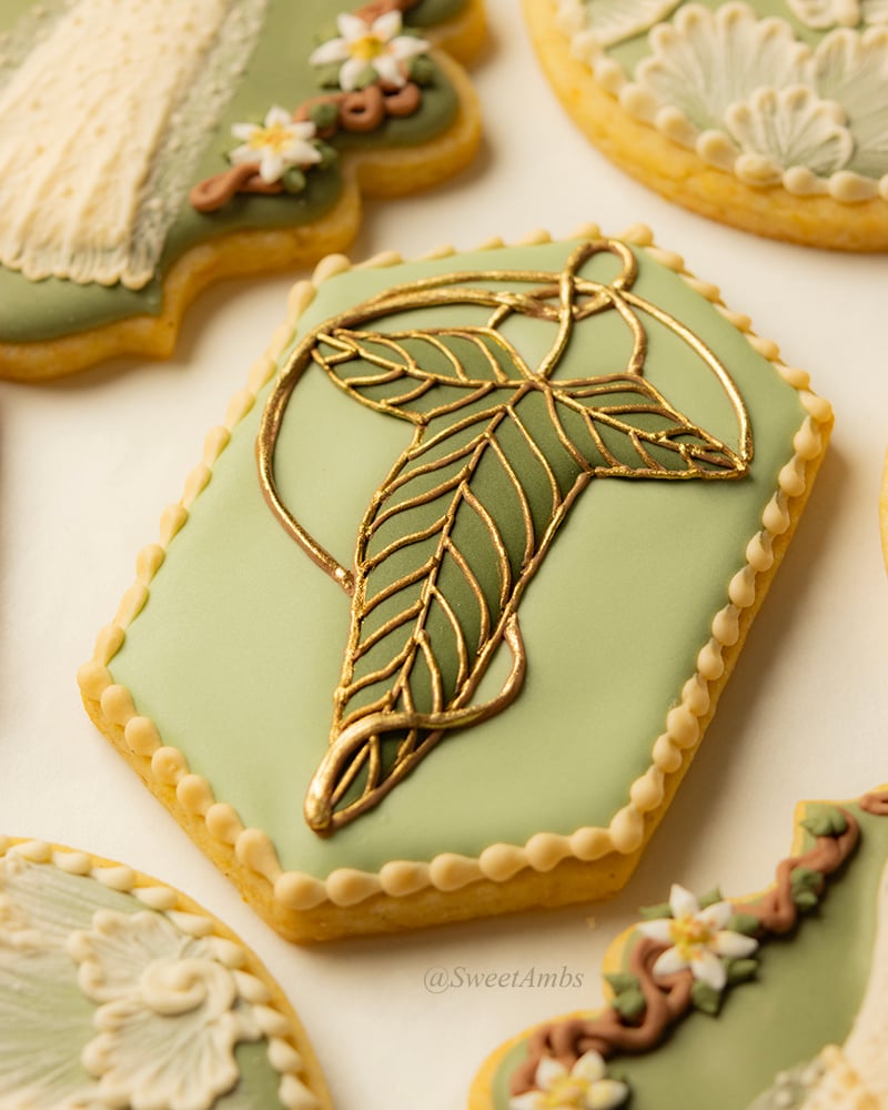 An elongated hexagon shaped cookie decorated with a royal icing ivy leaf brooch to resemble the one from Lord of the Rings.