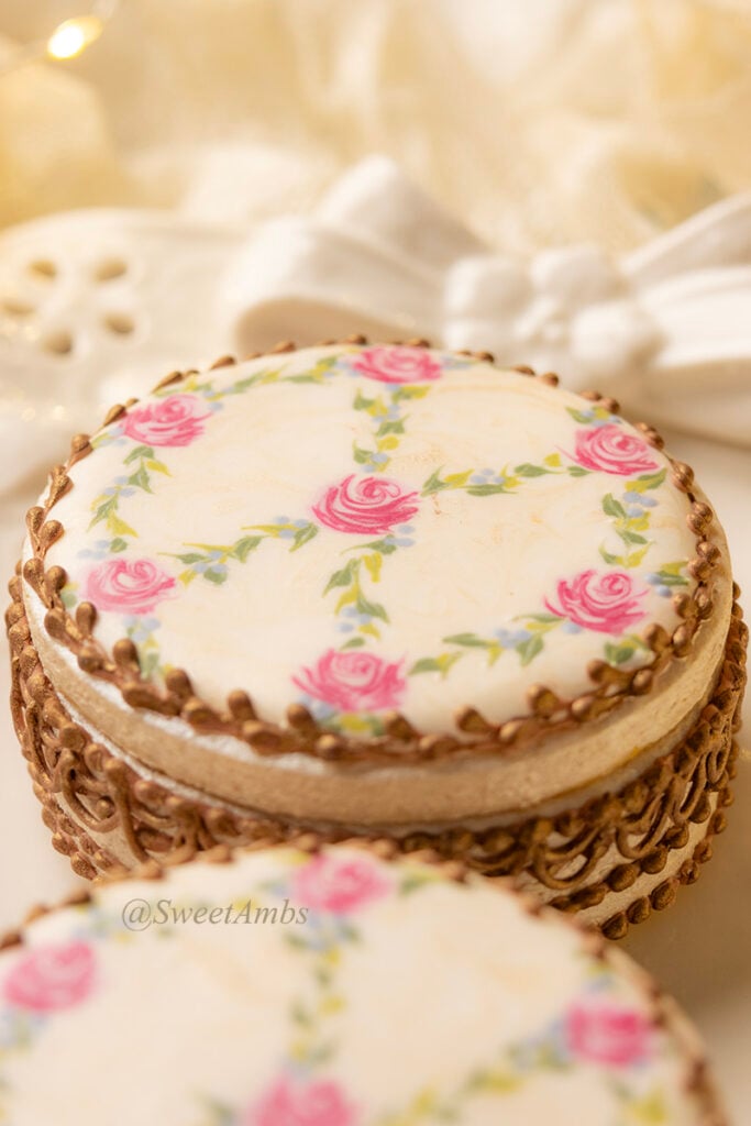 Cookies decorated to resemble vintage floral enameled makeup compacts. The cookie boxes are on a platter that has an eyelet lace edge and a ceramic bow.