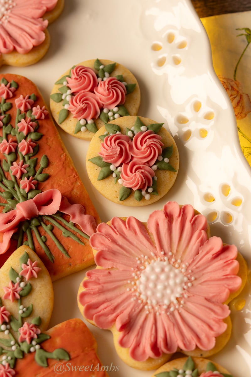 A set of floral cookies decorated in peach and terra cotta royal icing with green leaves. The cookies are on a platter with an eyelet lace edge.