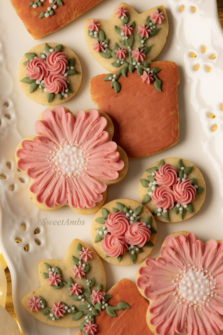 A set of floral cookies decorated in peach and terra cotta royal icing with green leaves. The cookies are on a platter with an eyelet lace edge.