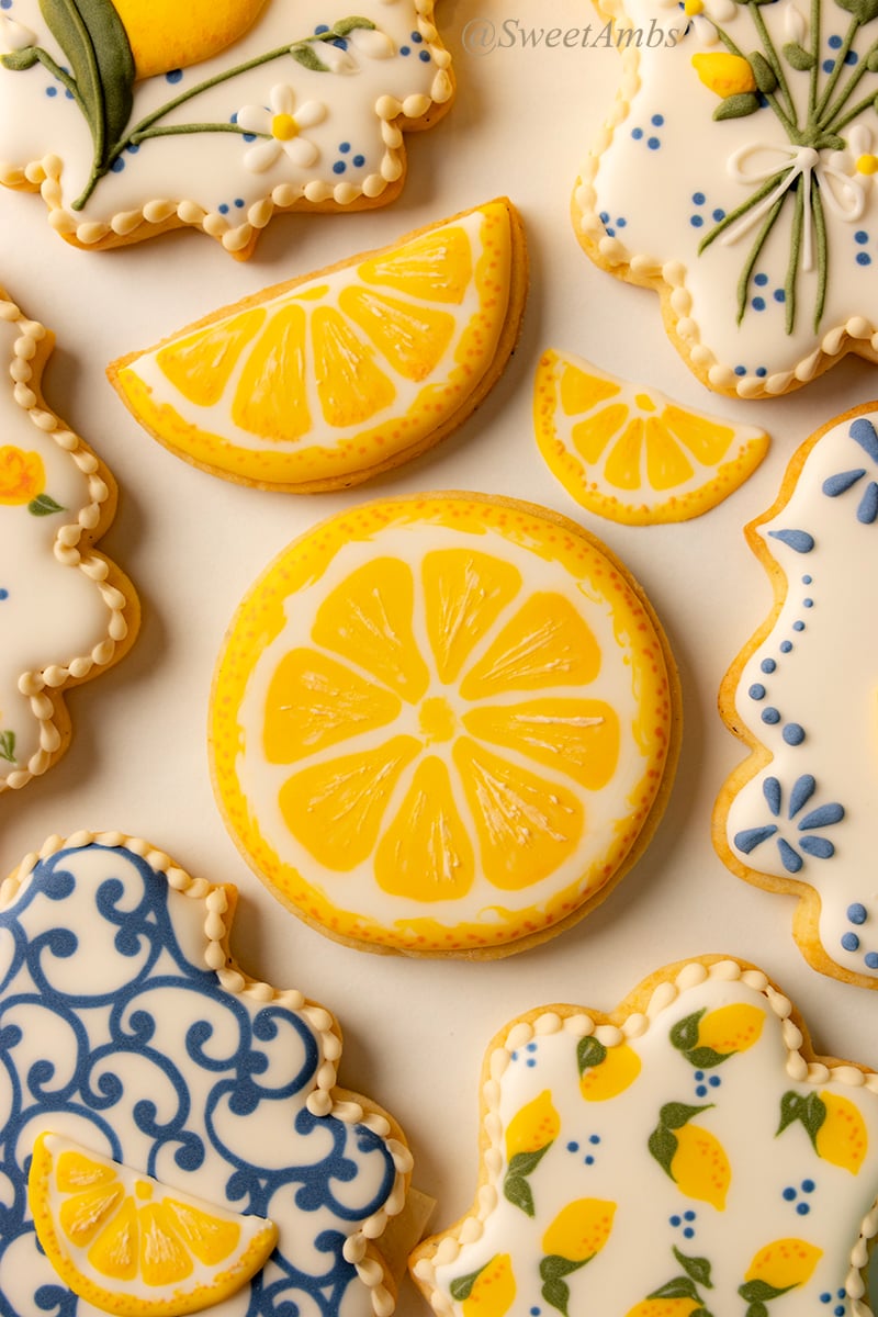 Cookies decorated to look like lemon slices and lemon wedges. The cookies are surrounded by plaque shaped cookies decorated with lemon-themed designs.